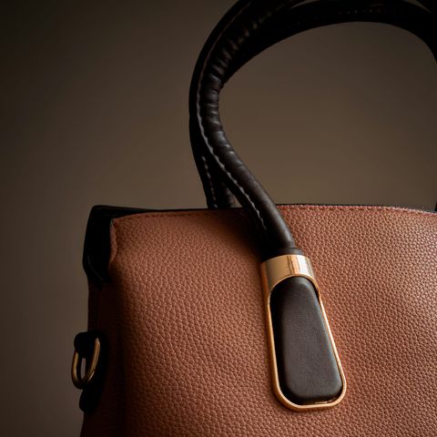 Close-up of a brown leather handbag with a black handle and gold-toned trim