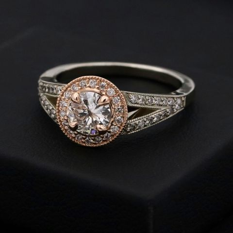 A diamond ring with a rose-gold halo of small diamonds, resting on a dark box